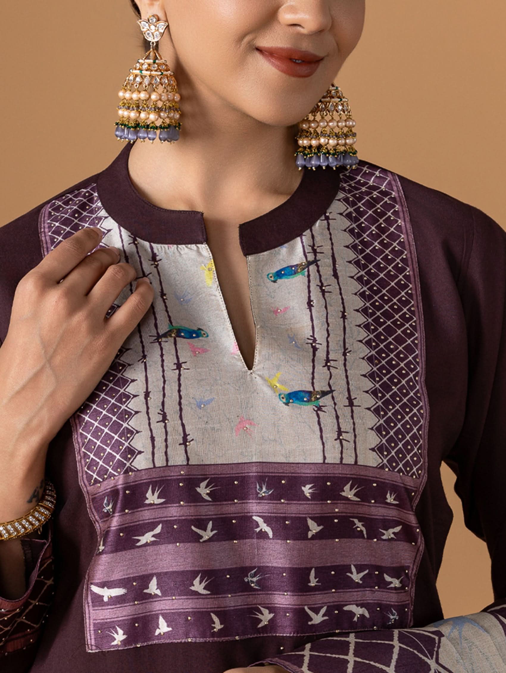 Woman wearing a traditional outfit with intricate patterns and gold earrings on a beige background
