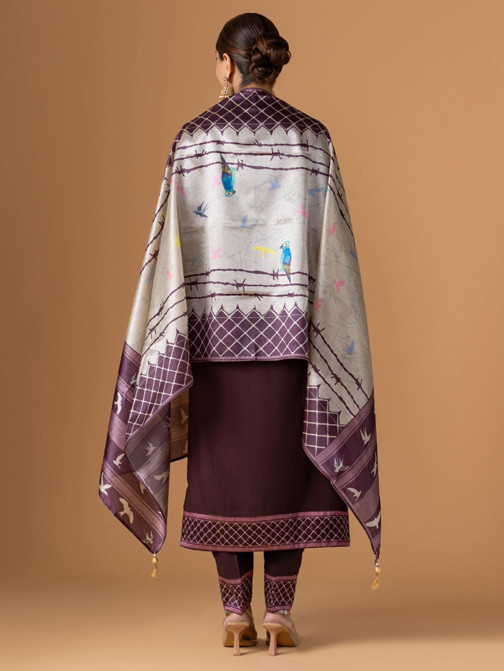 Woman wearing a patterned shawl over a traditional outfit against a beige background