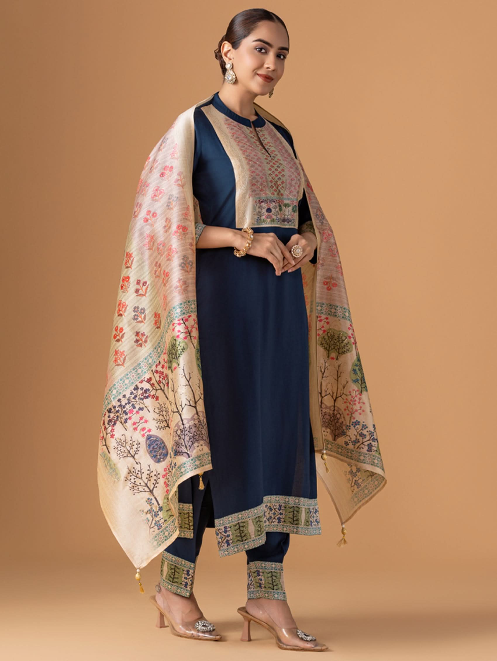 Woman wearing a navy blue traditional outfit with a floral shawl on a beige background
