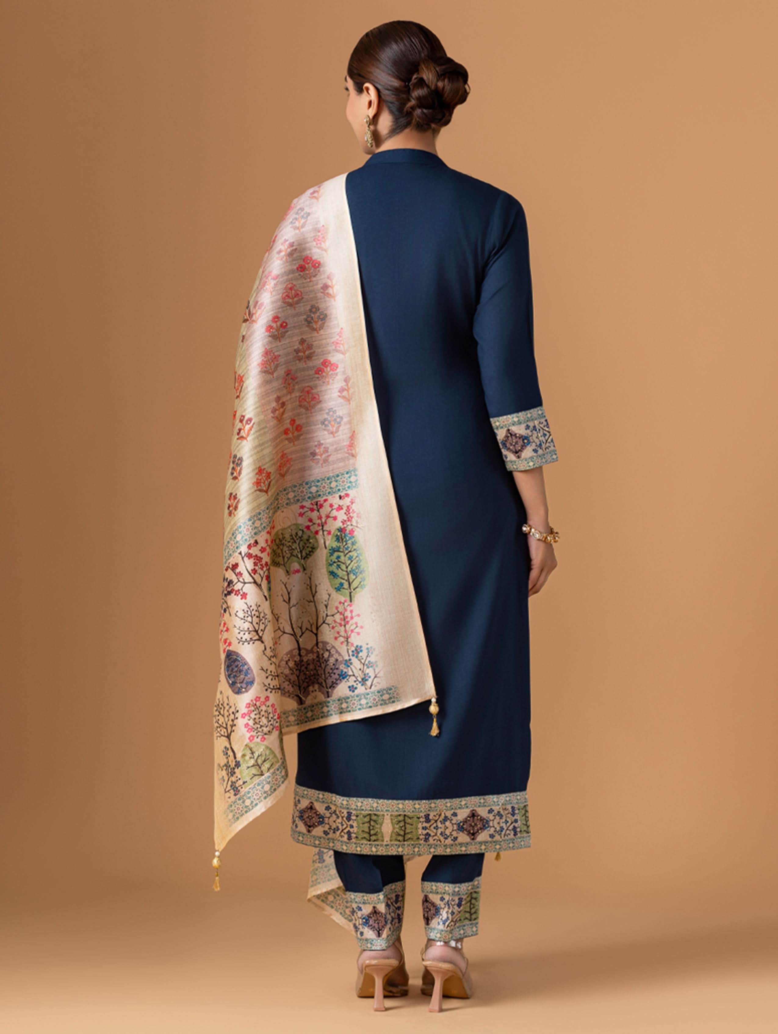 Woman wearing a navy blue traditional outfit with a floral shawl on a beige background