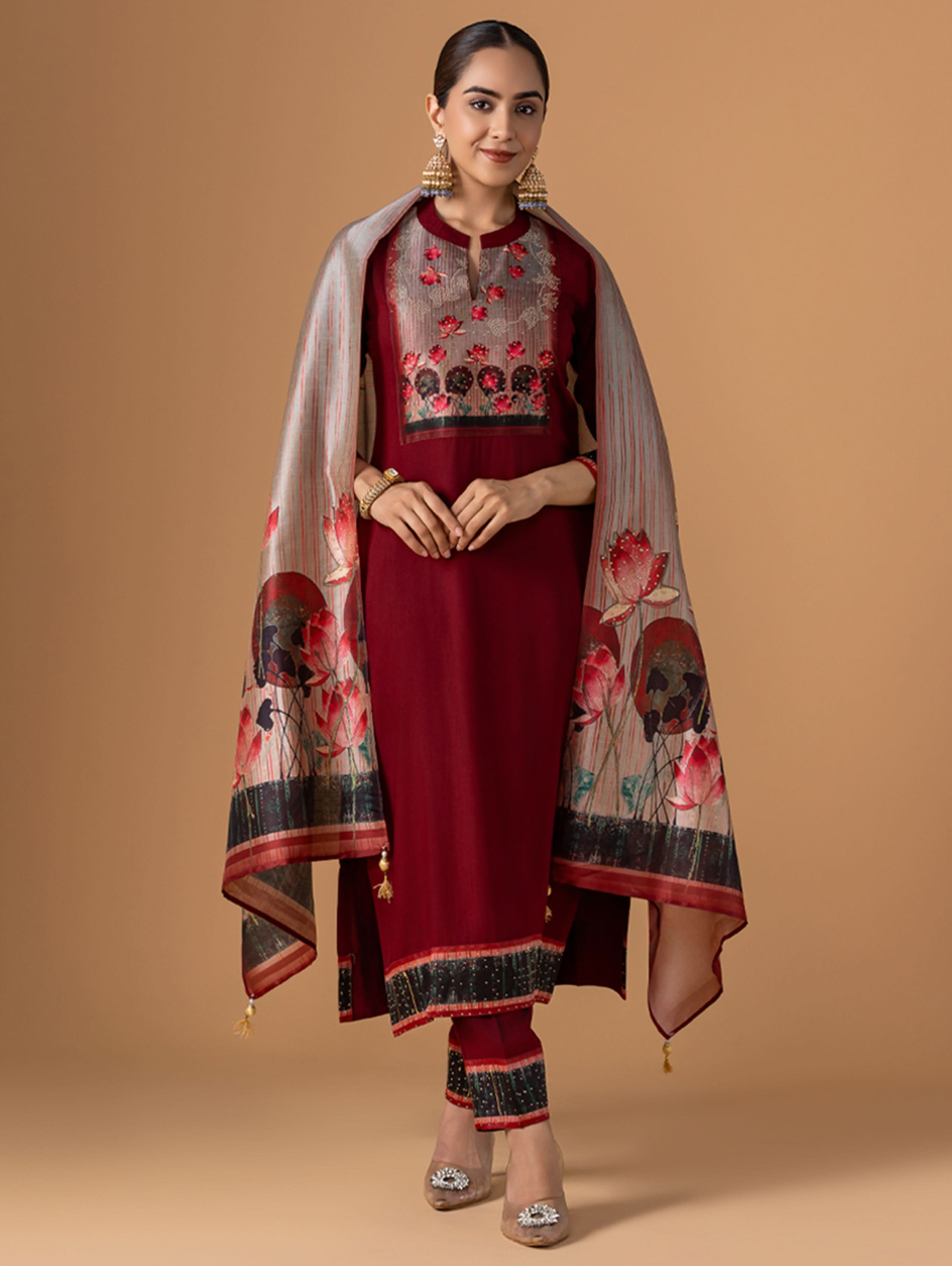 Woman wearing a maroon traditional outfit with a floral shawl on a beige background