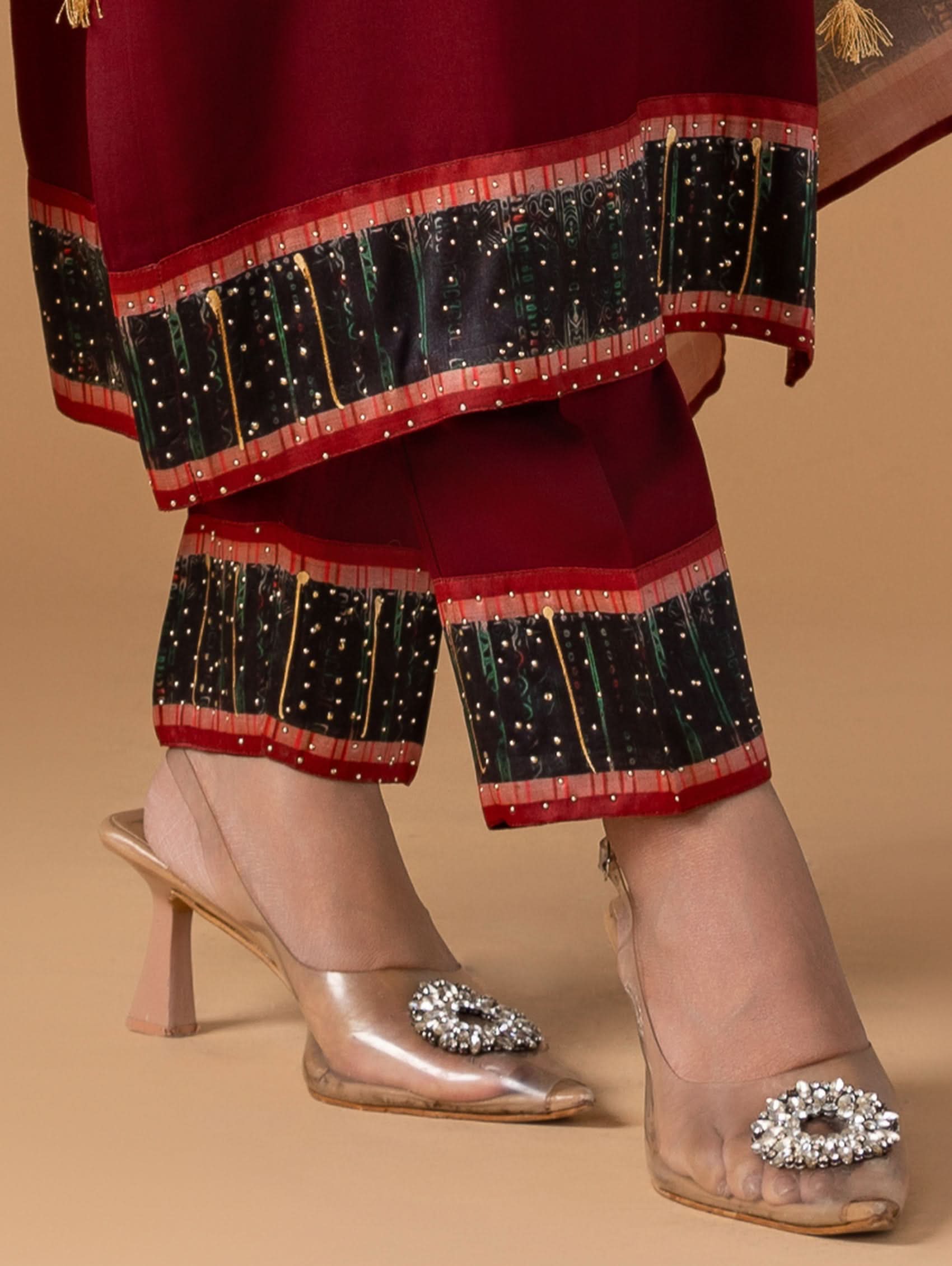 Traditional outfit with red and black patterned fabric and transparent high-heeled shoes with embellishments on a beige background.