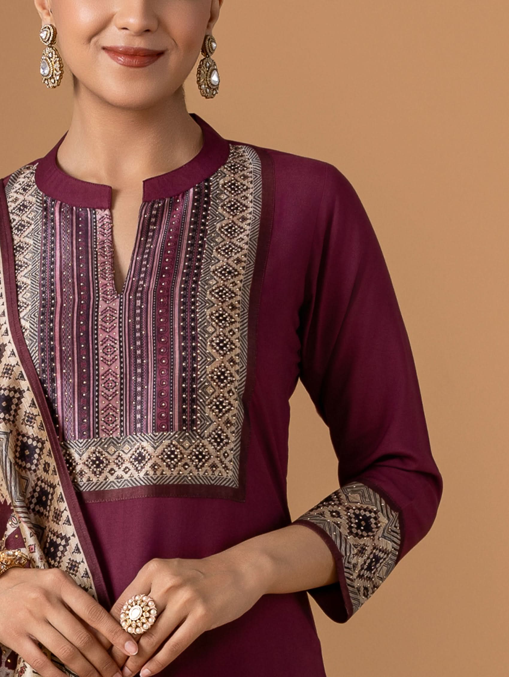 Woman wearing a maroon traditional outfit with intricate patterns on a beige background