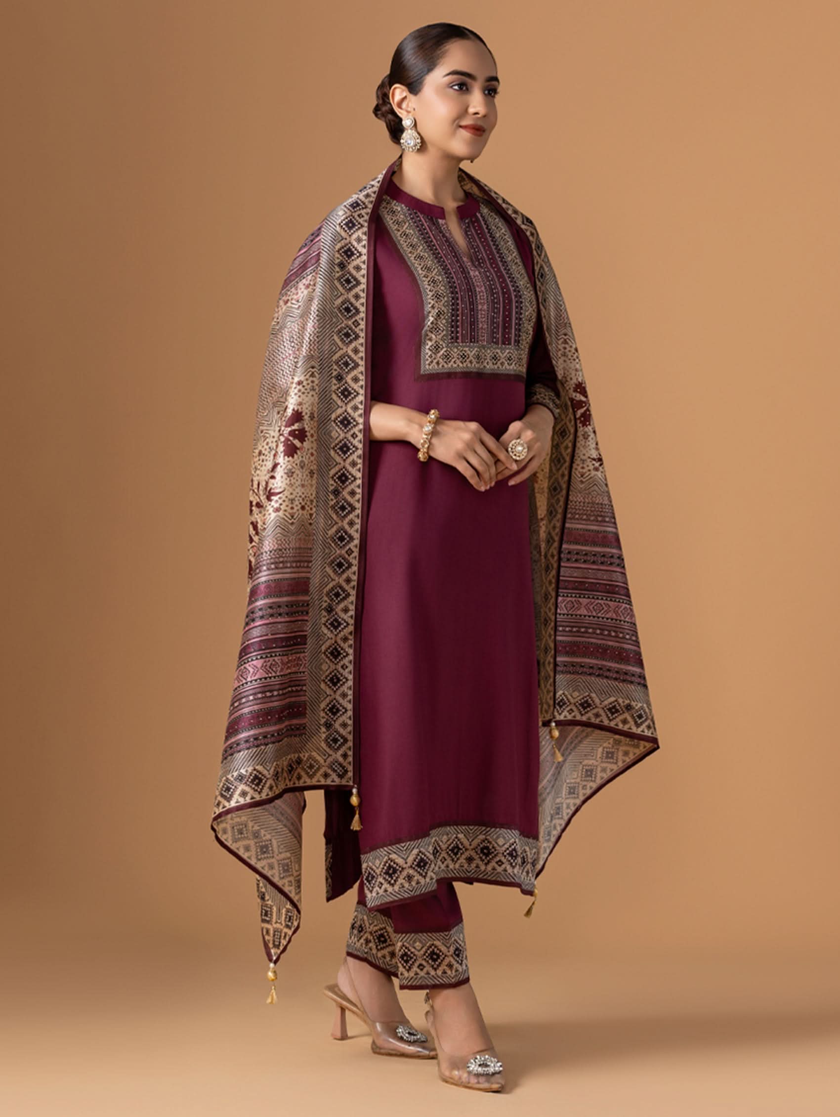 Woman wearing a maroon traditional outfit with a patterned shawl on a beige background