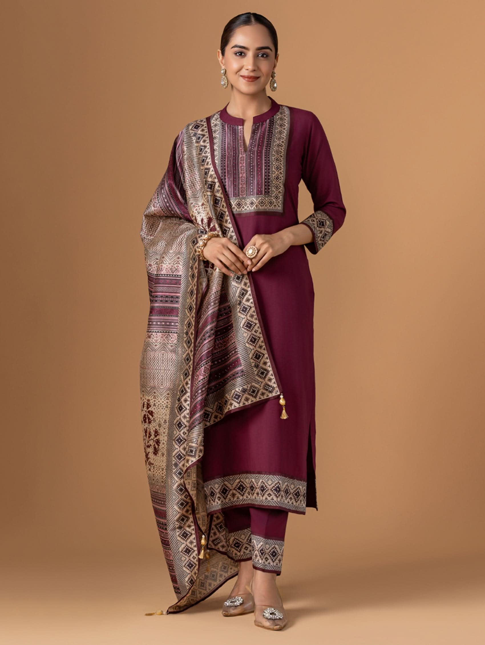 Woman wearing a maroon traditional outfit with a patterned dupatta on a beige background