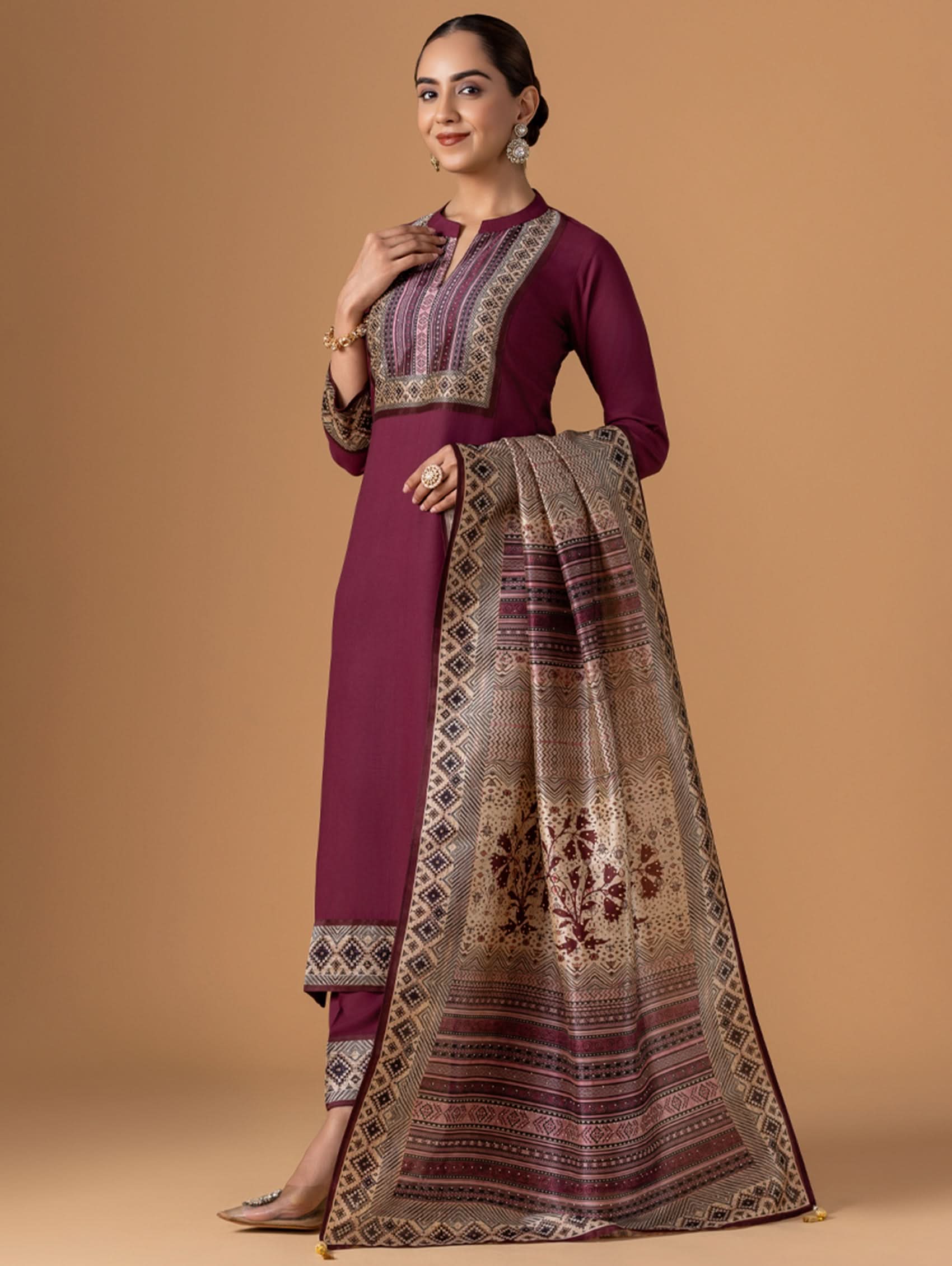 Woman wearing a maroon traditional outfit with a patterned scarf on a beige background