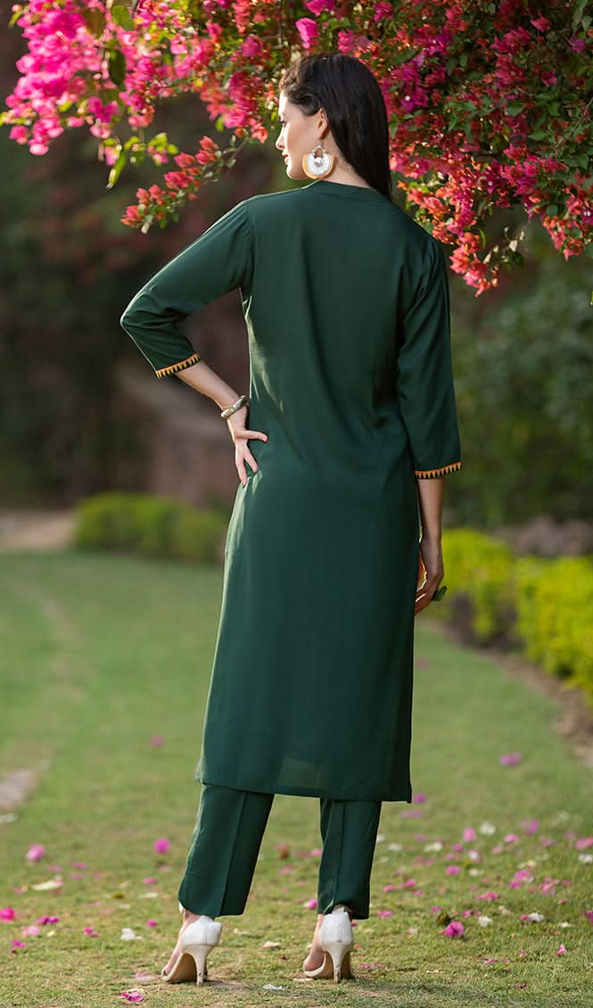 Woman in a green outfit standing in a garden with pink flowers and greenery.