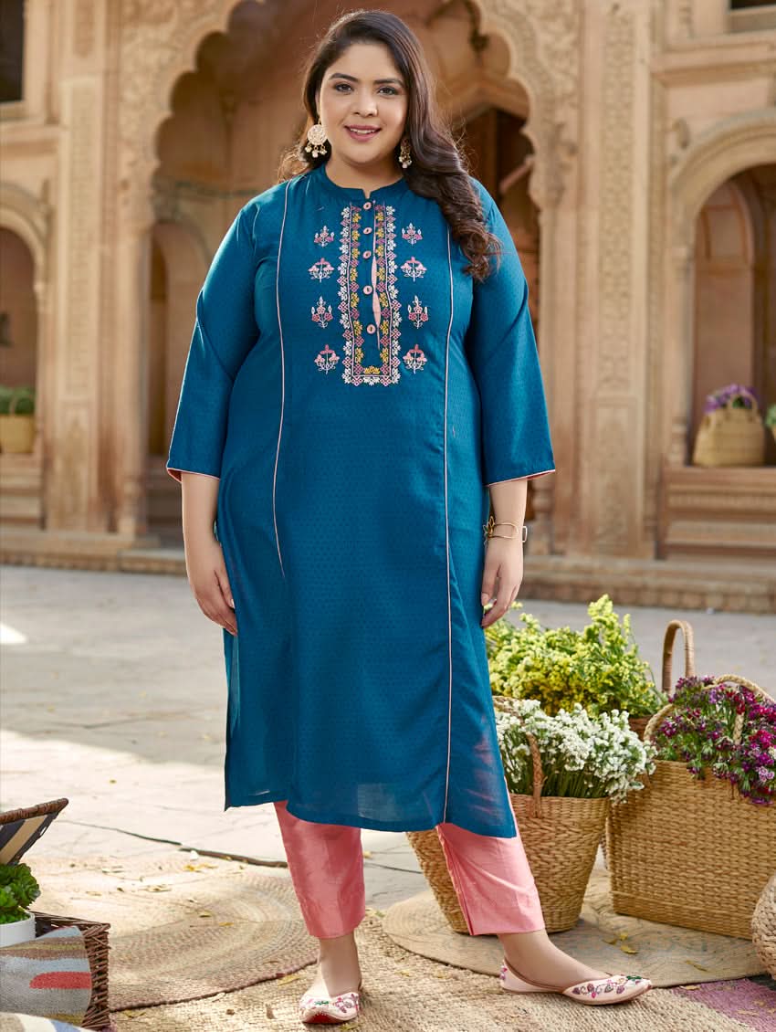 A woman standing in a beautifully decorated outdoor setting wearing a blue chunan kurta with embroidered details and three-fourth sleeves, paired with pink pants.