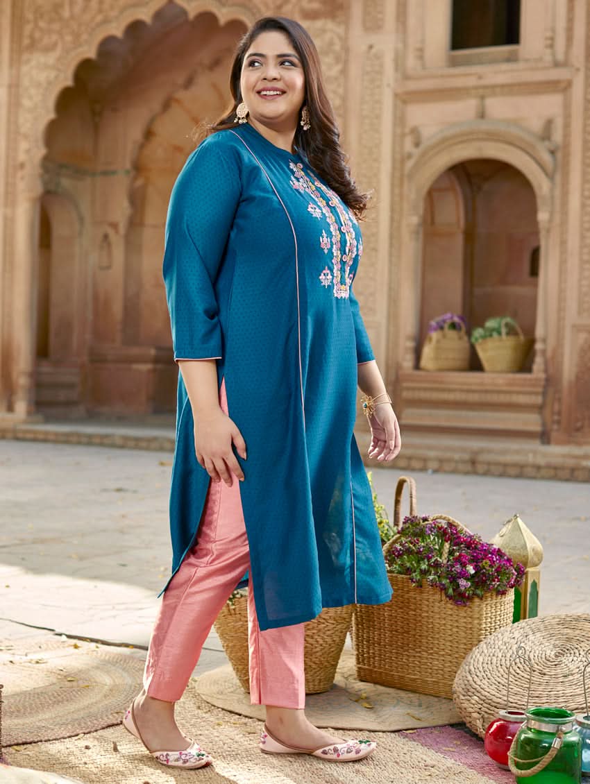 A woman standing in a beautifully decorated outdoor setting wearing a blue chunan kurta with embroidered details and three-fourth sleeves, paired with pink pants.