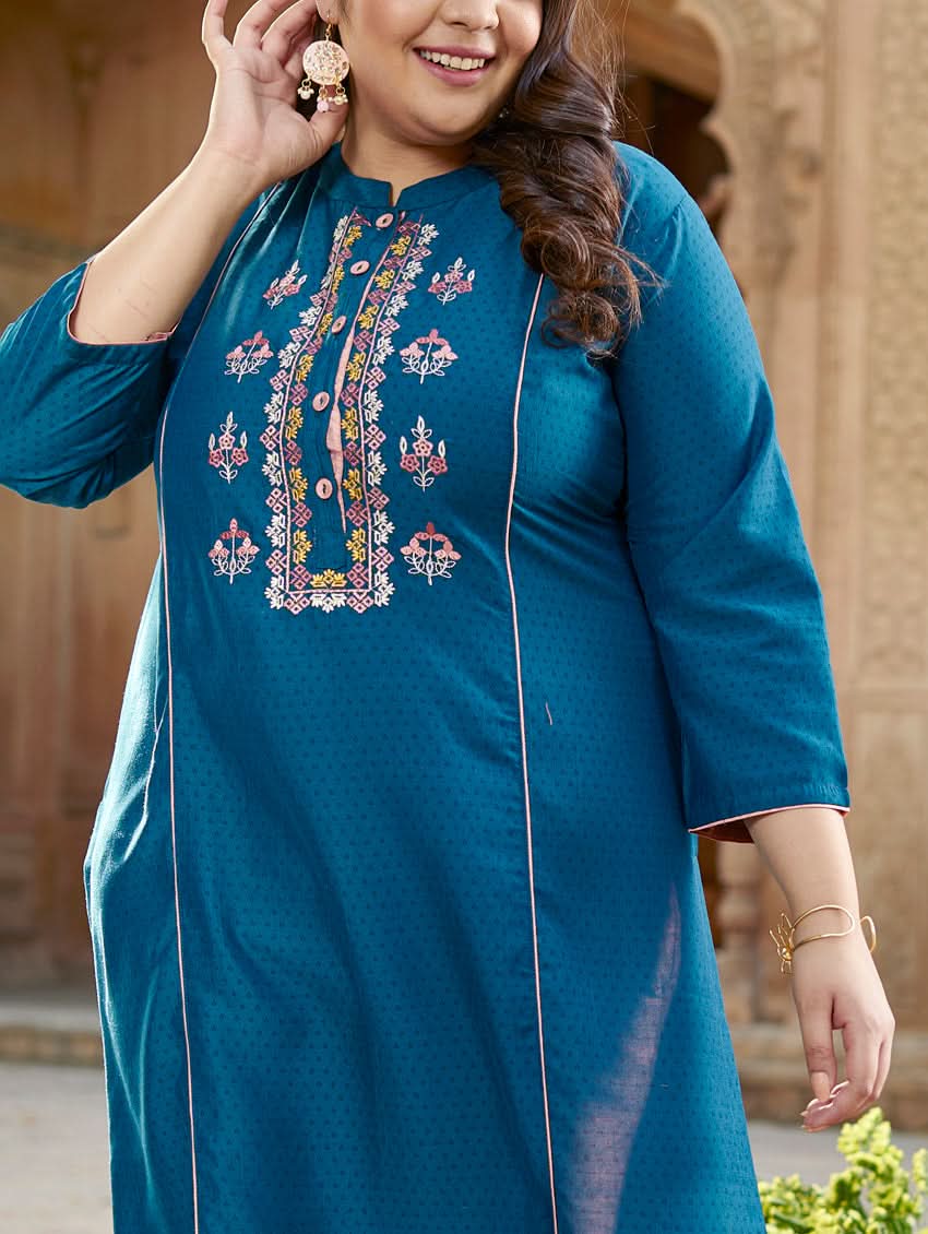 A woman standing in a beautifully decorated outdoor setting wearing a blue chunan kurta with embroidered details and three-fourth sleeves, paired with pink pants.