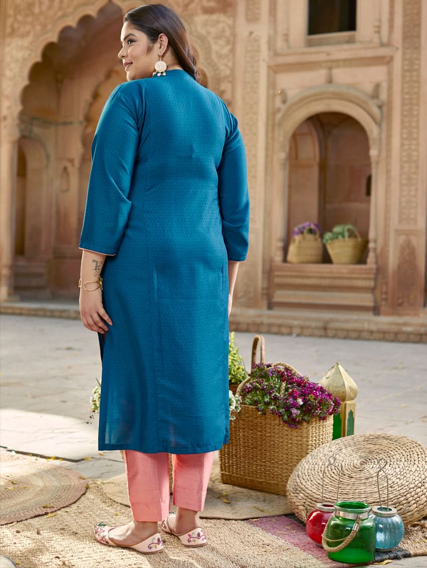 A woman standing in a beautifully decorated outdoor setting wearing a blue chunan kurta with embroidered details and three-fourth sleeves, paired with pink pants.