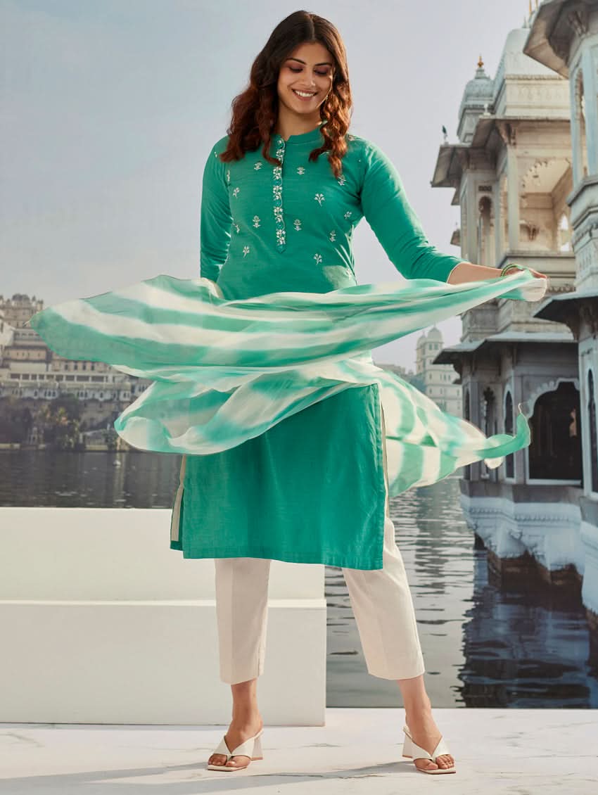 A woman wearing a solid-coloured cotton kurta with pants and a printed shiffon dupatta, standing against a backdrop of a traditional Indian palace.