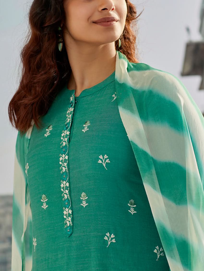 A woman wearing a solid-coloured cotton kurta with pants and a printed shiffon dupatta, standing against a backdrop of a traditional Indian palace.
