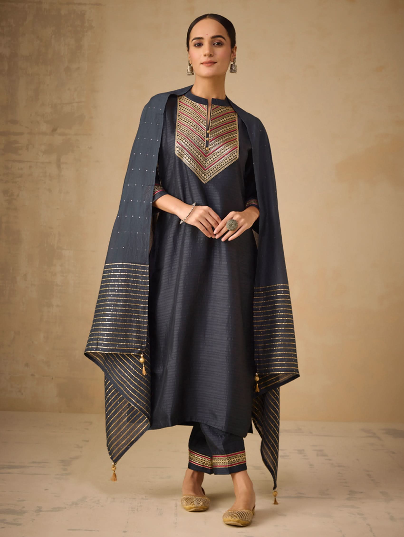 Woman wearing a traditional outfit with a dark blue dress and matching cape against a beige background