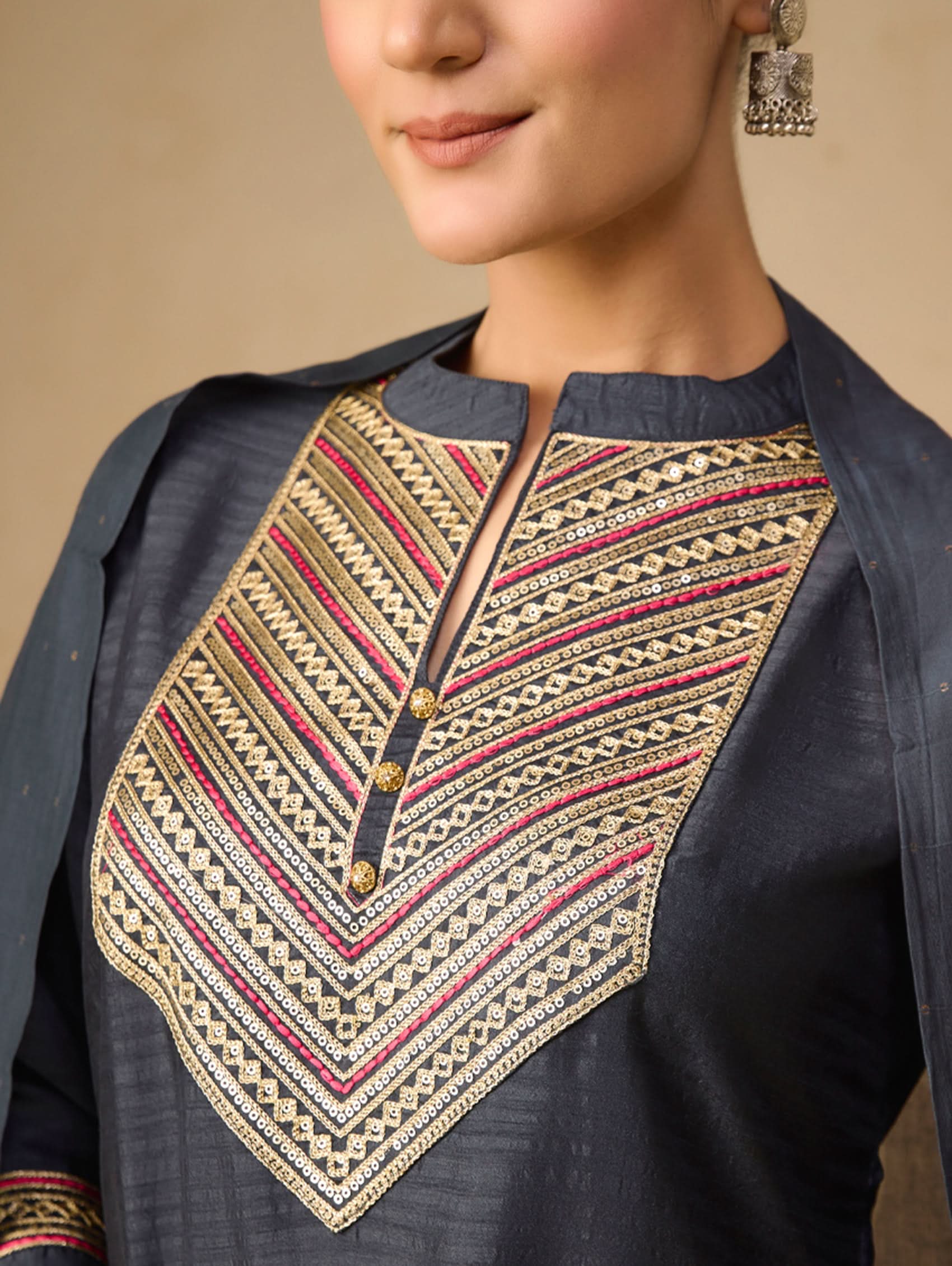 Close-up of a person wearing a dark blue embroidered top with geometric patterns on a beige background