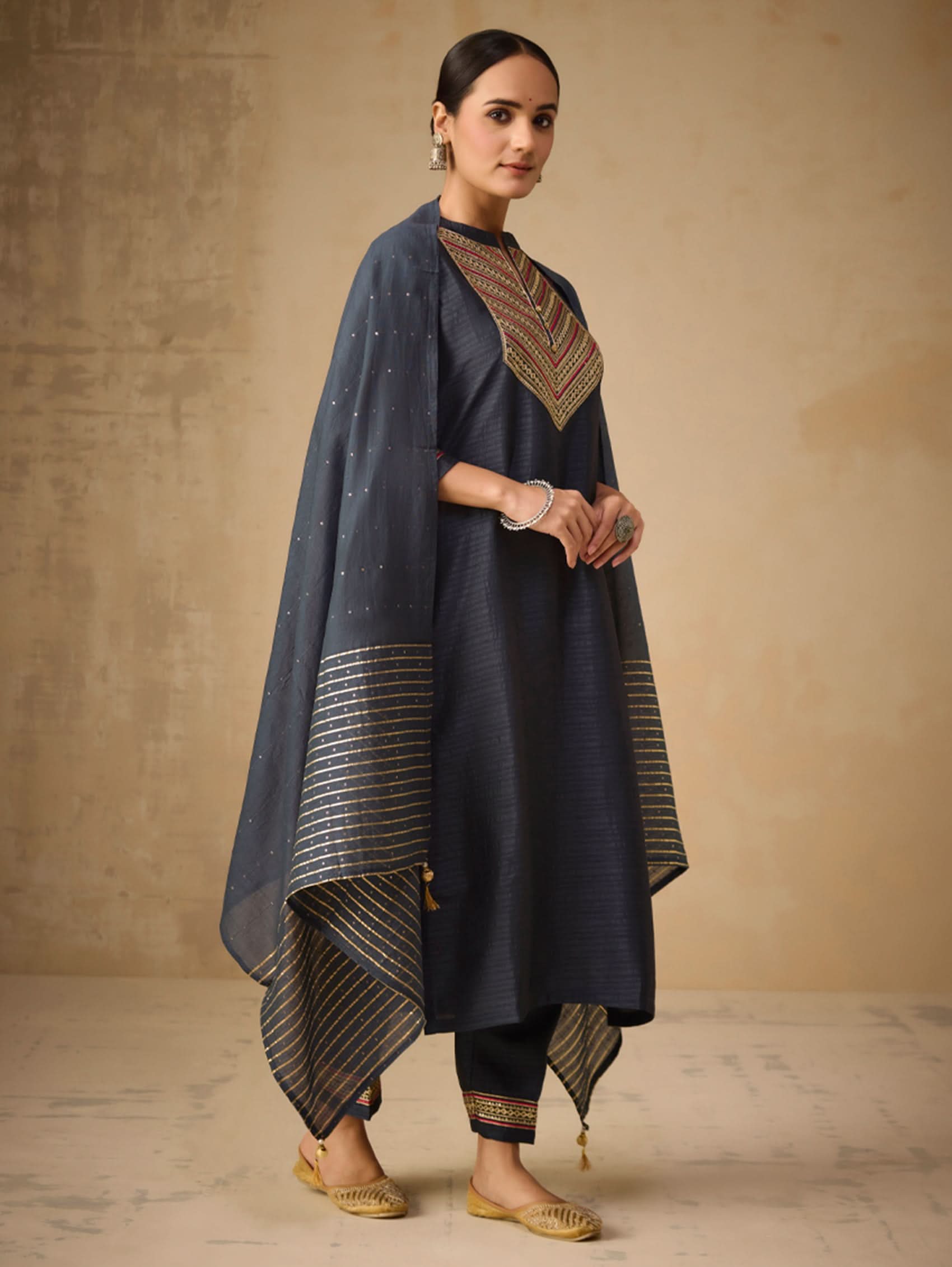 Woman wearing a dark blue traditional outfit with gold accents against a beige background