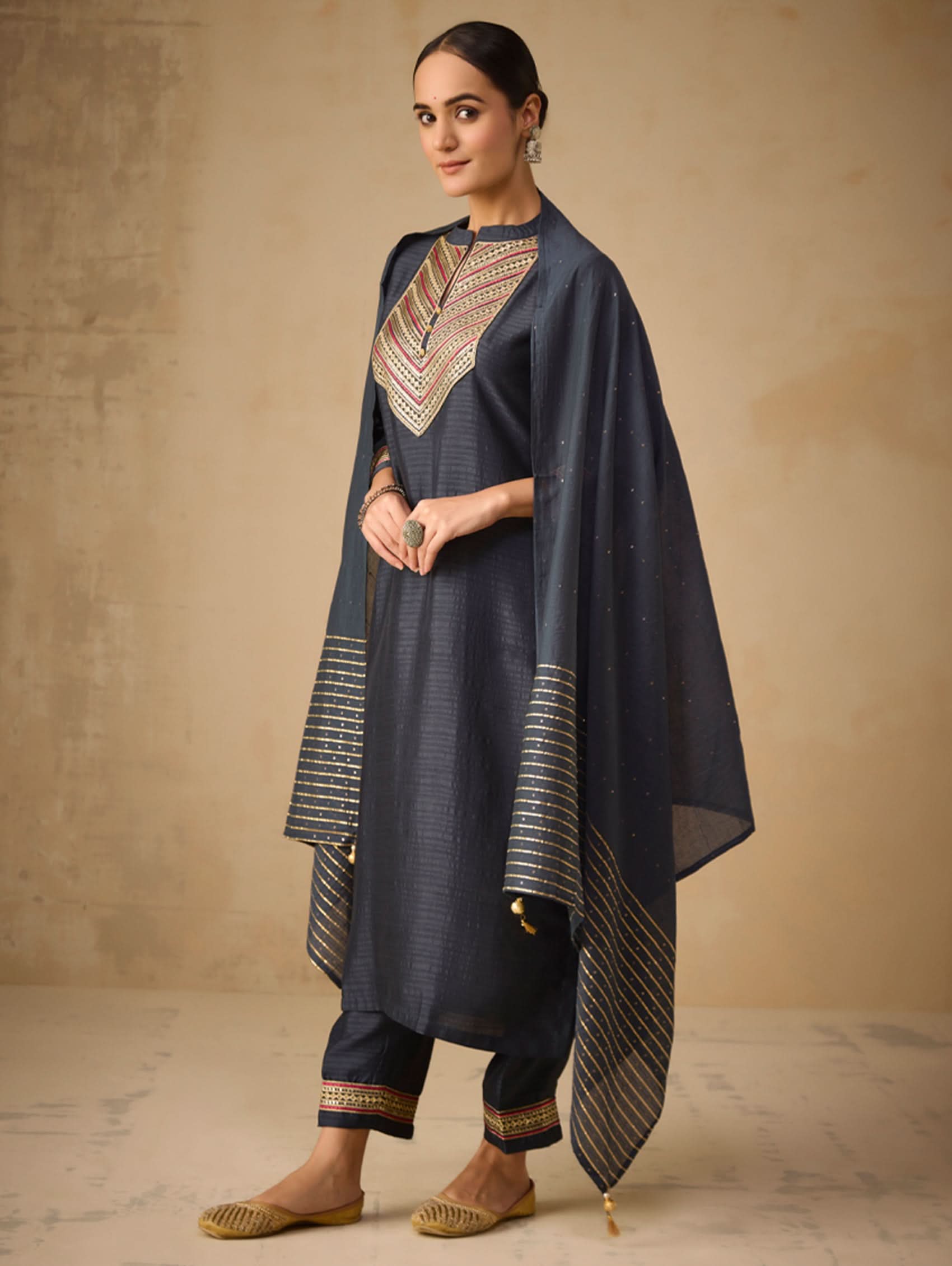 Woman wearing a dark blue traditional outfit with gold accents against a beige background