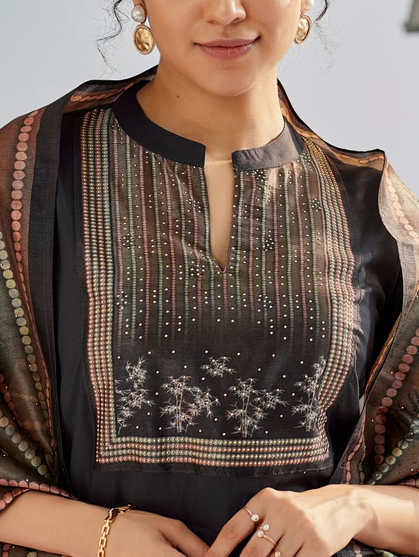 A woman wearing a traditional suit set with a kurta, pants, and a dupatta, standing near a historical building with a body of water in the background.
