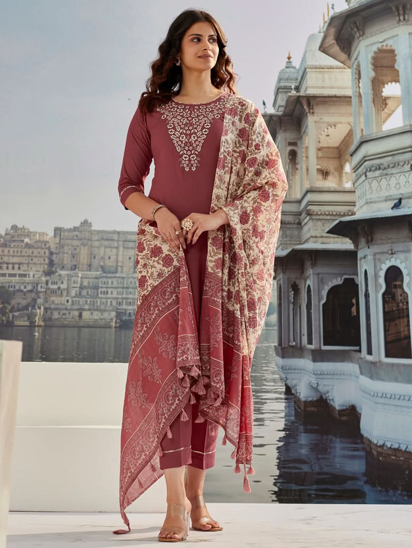 A woman wearing a solid-coloured rayon kurta with pants and a printed mul dupatta, standing against a backdrop of a traditional Indian palace.