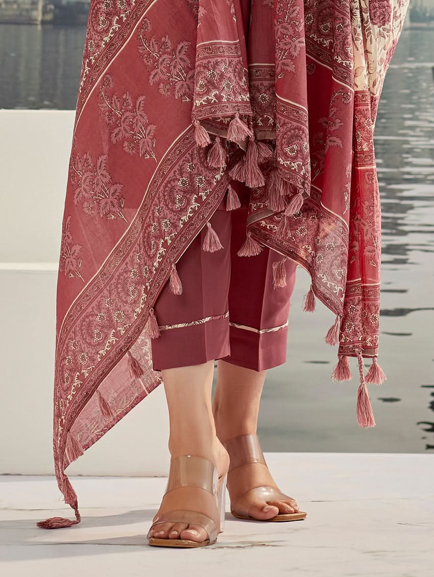 A woman wearing a solid-coloured rayon kurta with pants and a printed mul dupatta, standing against a backdrop of a traditional Indian palace.