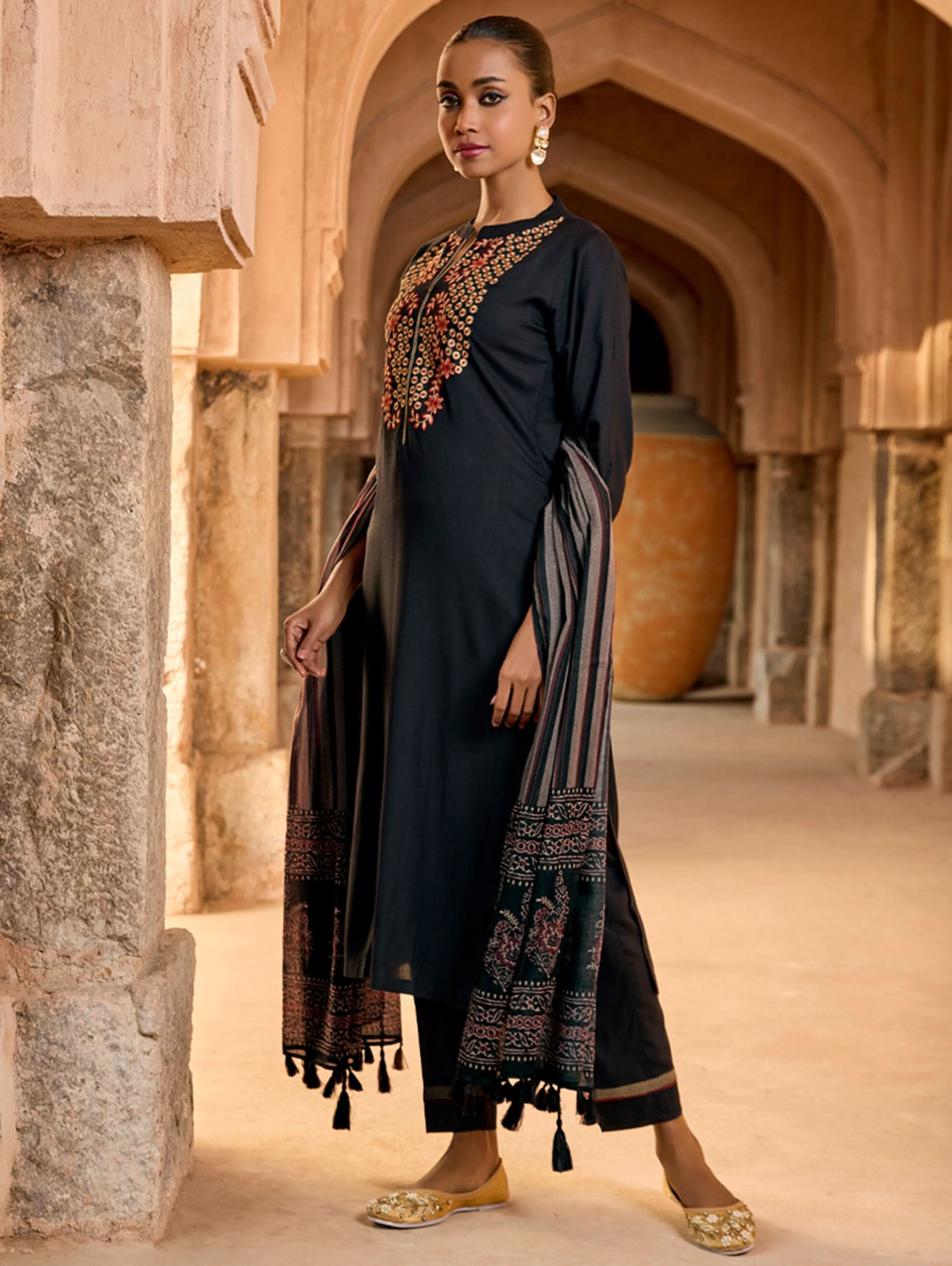A woman wearing a black viscose rayon suit set with embroidery, consisting of a kurta and pants, and a printed dupatta.