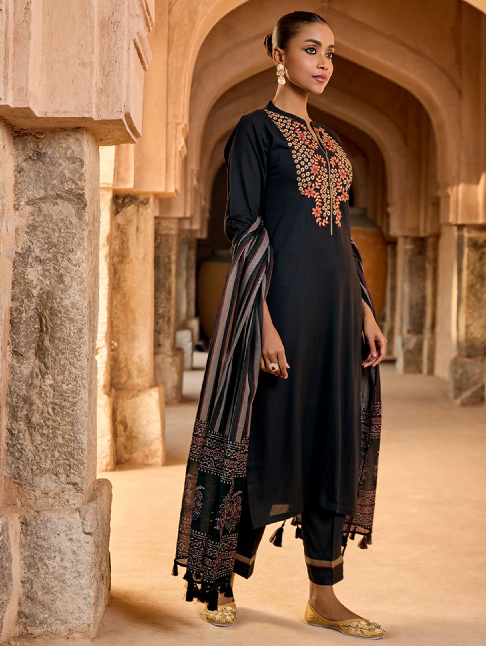 A woman wearing a black viscose rayon suit set with embroidery, consisting of a kurta and pants, and a printed dupatta.