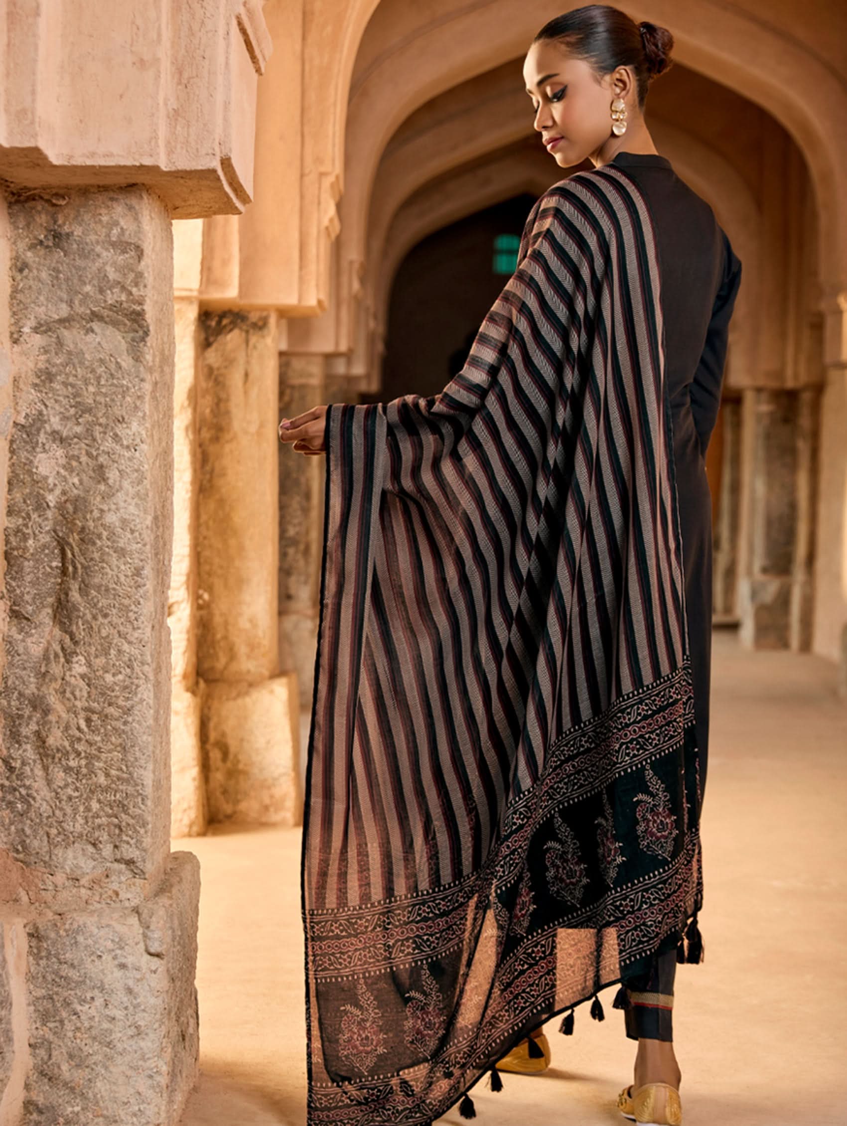 A woman wearing a black viscose rayon suit set with embroidery, consisting of a kurta and pants, and a printed dupatta.
