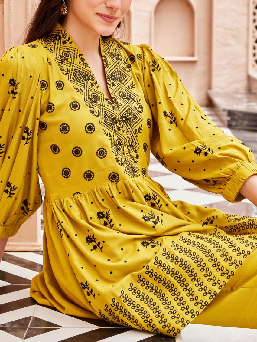 A woman standing on a balcony wearing an embroidered Yellow kurta set with V-neckline and three-quarter sleeves, paired with black pants with a partially elasticated waistband and pockets on either side.