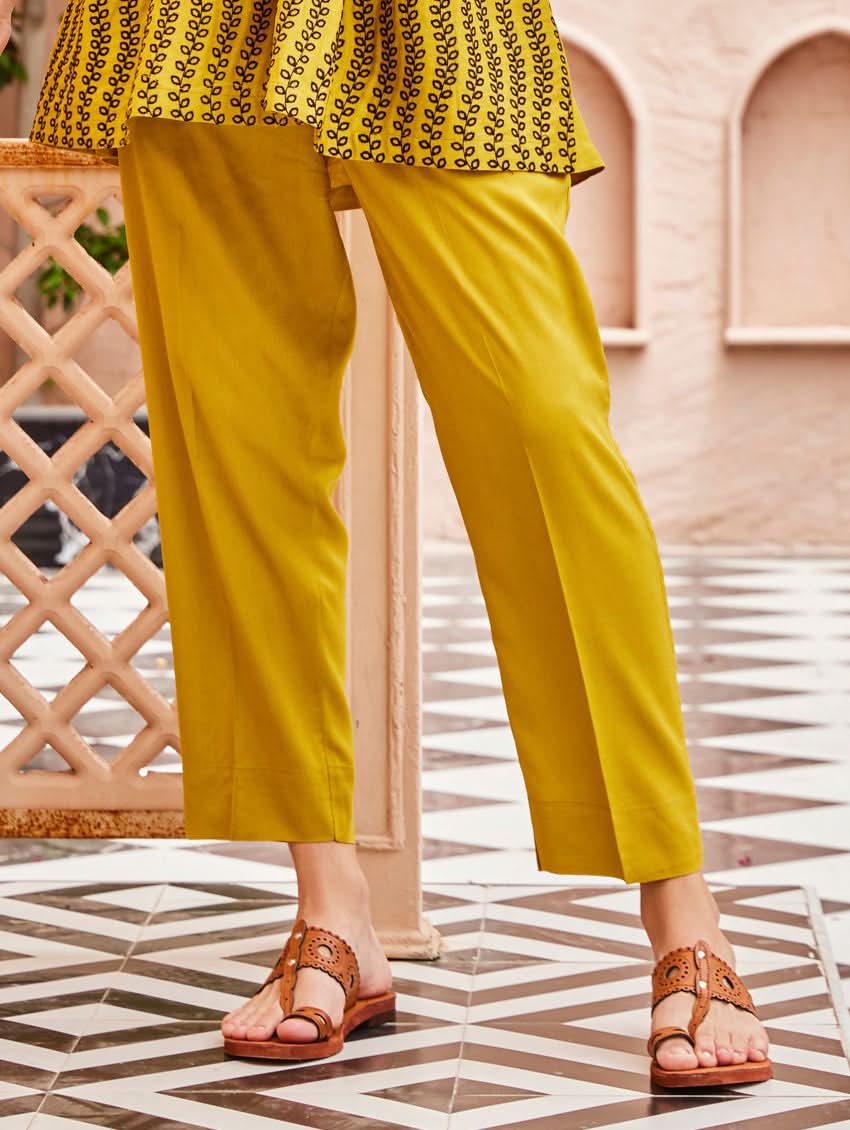 A woman standing on a balcony wearing an embroidered Yellow kurta set with V-neckline and three-quarter sleeves, paired with black pants with a partially elasticated waistband and pockets on either side.