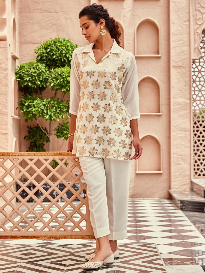A woman standing beautiful studio wearing a white embellished viscose flex co-ord set with short kurta and pants,