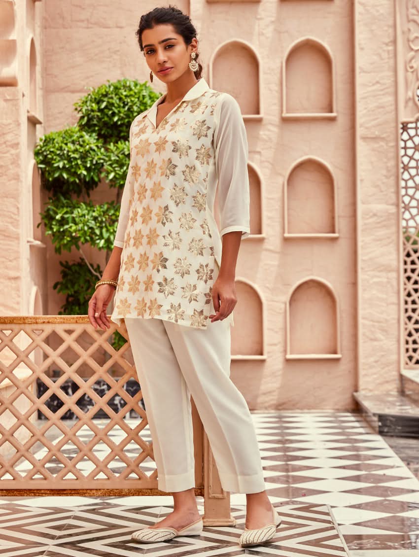 A woman standing beautiful studio wearing a white embellished viscose flex co-ord set with short kurta and pants,
