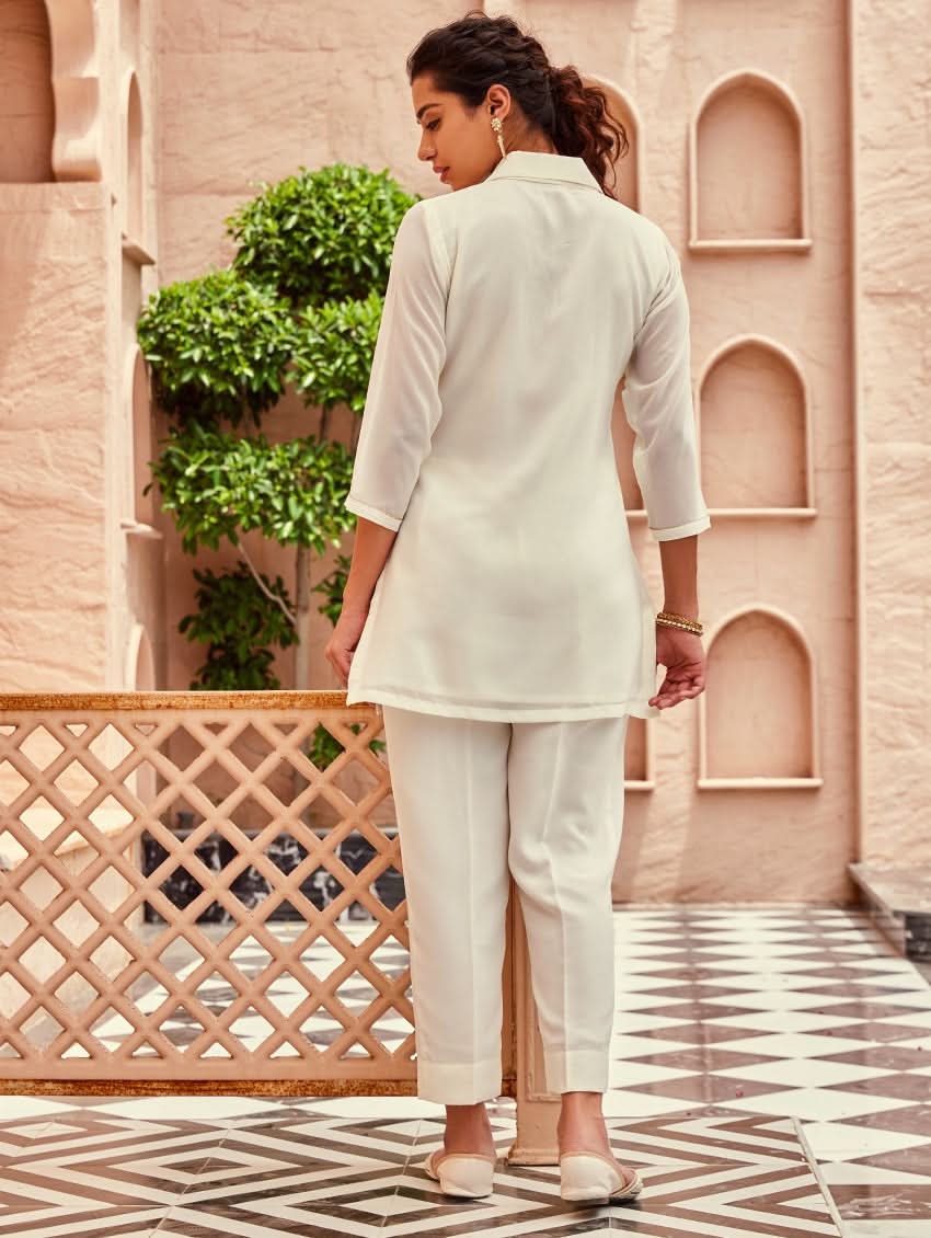 A woman standing beautiful studio wearing a white embellished viscose flex co-ord set with short kurta and pants,