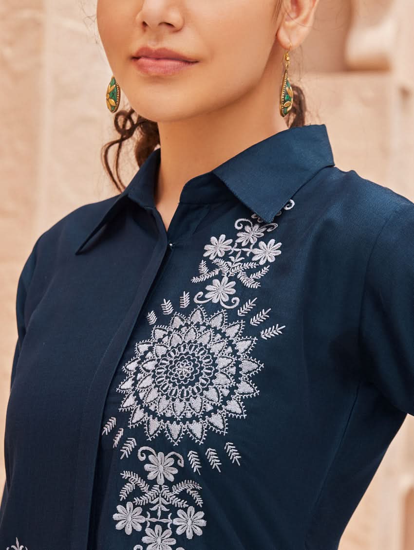 A woman standing outdoors wearing an embroidered viscose rayon co-ord set with a rever neckline, three-quarter sleeves, and pockets on either side.