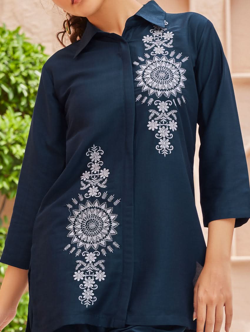 A woman standing outdoors wearing an embroidered viscose rayon co-ord set with a rever neckline, three-quarter sleeves, and pockets on either side.