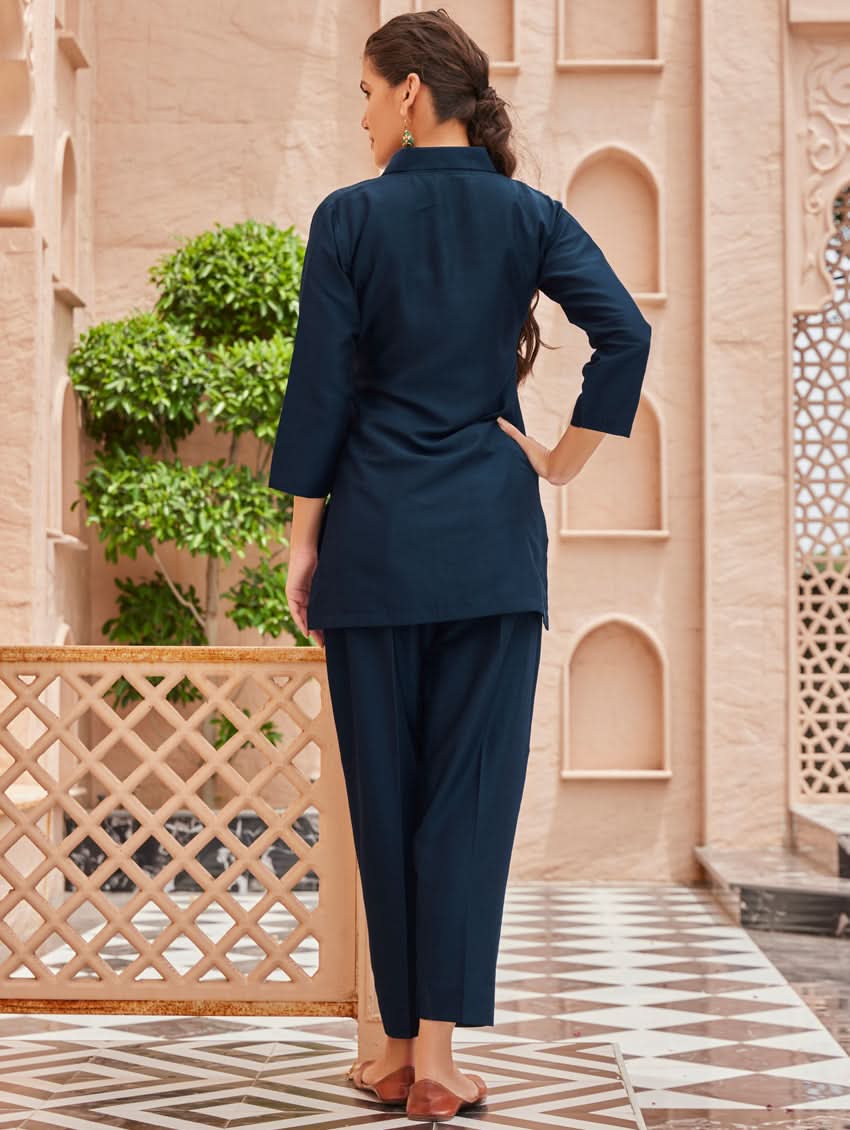 A woman standing outdoors wearing an embroidered viscose rayon co-ord set with a rever neckline, three-quarter sleeves, and pockets on either side.