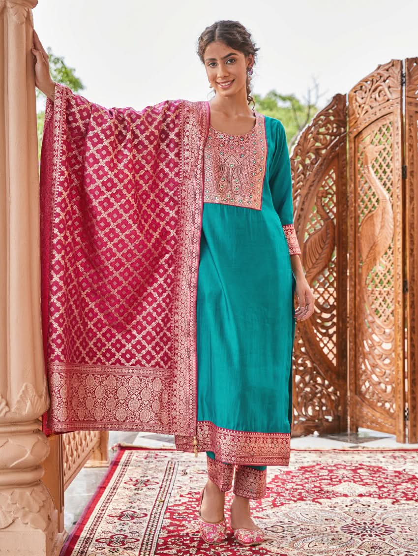 A woman standing in a traditional setting, wearing a blue silk suit with embroidered details and a dupatta with solid print and jacquard dupatta.