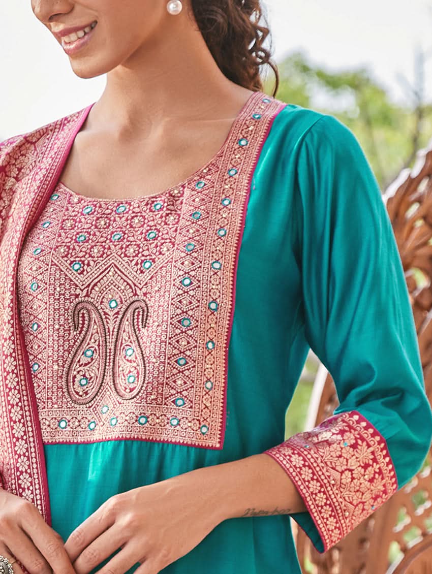A woman standing in a traditional setting, wearing a blue silk suit with embroidered details and a dupatta with solid print and jacquard dupatta.