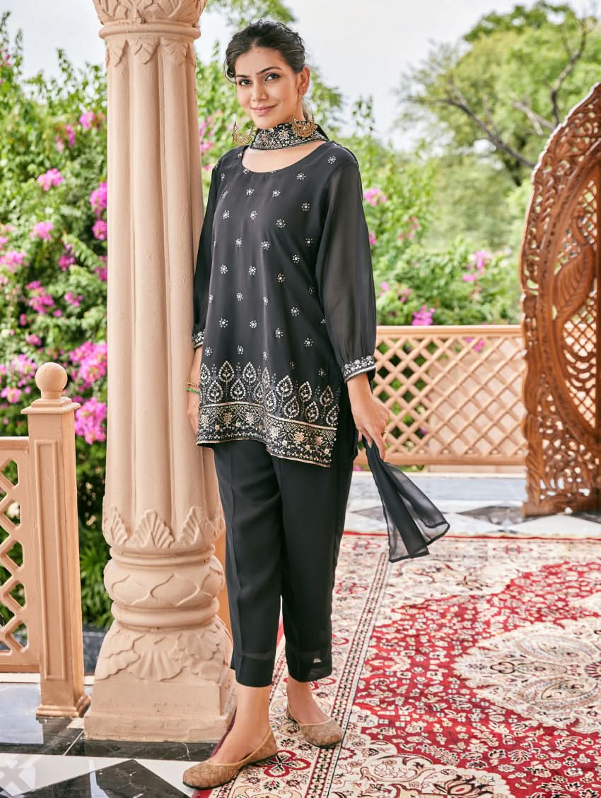 A woman standing outdoors wearing an embroidered georgette co-ord set with a round neckline, three-quarter sleeves, and pockets on either side. The set is predominantly black with embellishments in a sequin or computerized thread on the kurta.