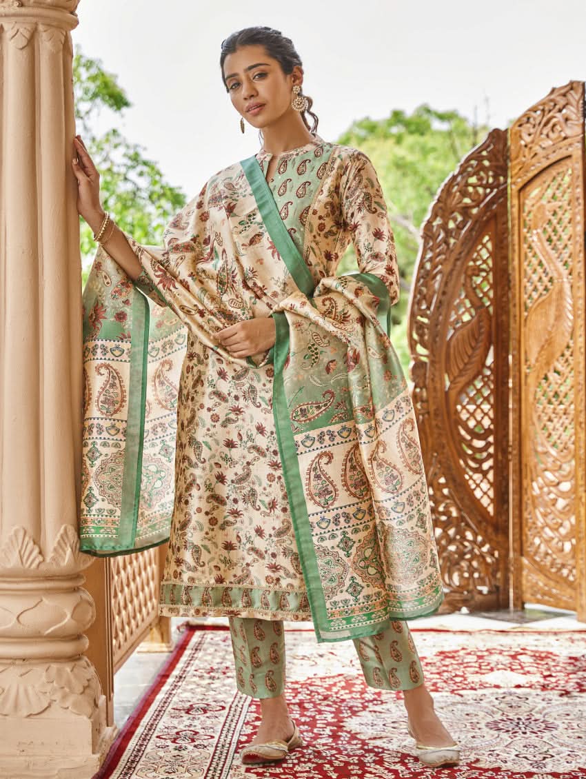 A woman standing in an ornate room wearing a traditional digital printed silk suit set with a dupatta, featuring floral and geometric patterns.