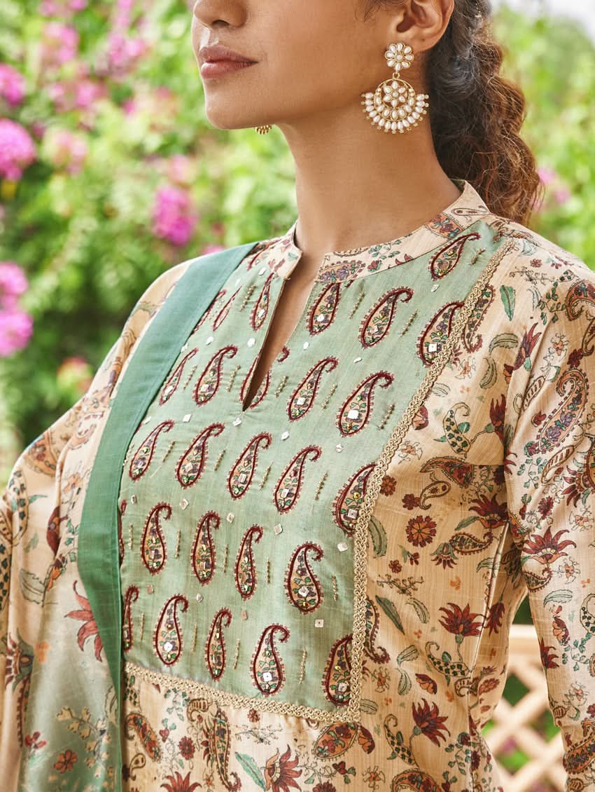 A woman standing in an ornate room wearing a traditional digital printed silk suit set with a dupatta, featuring floral and geometric patterns.