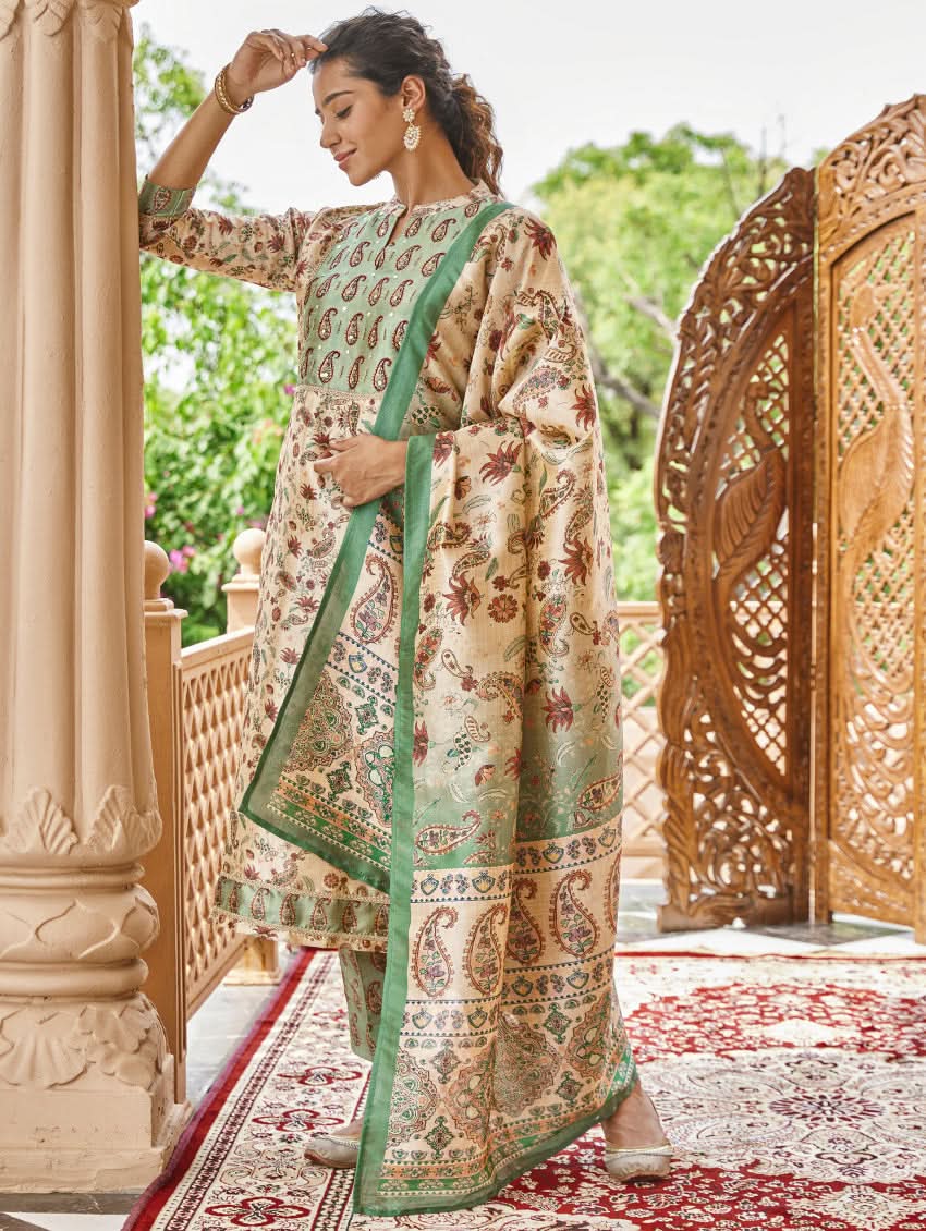 A woman standing in an ornate room wearing a traditional digital printed silk suit set with a dupatta, featuring floral and geometric patterns.