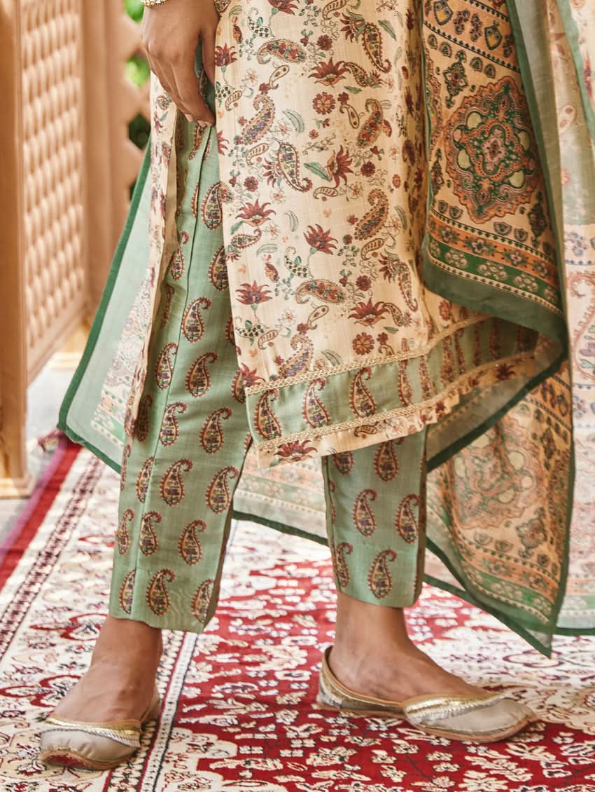 A woman standing in an ornate room wearing a traditional digital printed silk suit set with a dupatta, featuring floral and geometric patterns.
