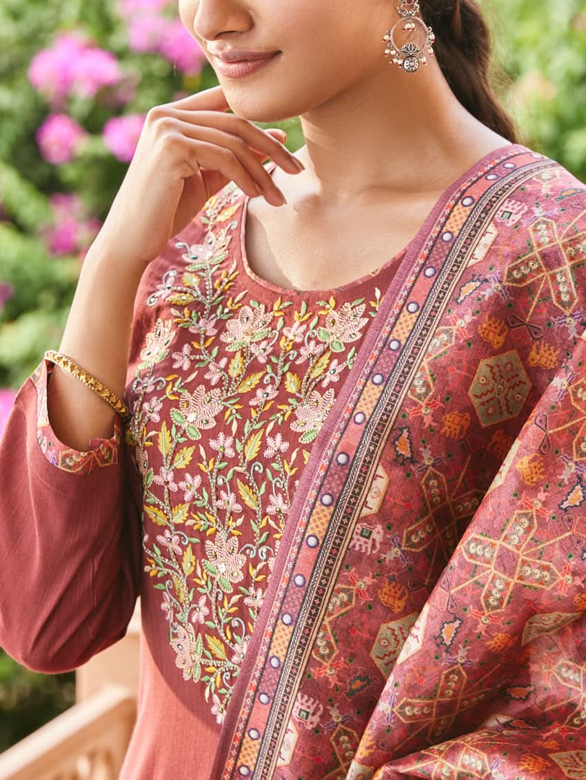 A woman standing in an elegant pose wearing a red silk suit set with floral patterns on the dupatta, straight pants, and a kurta with pearl work.