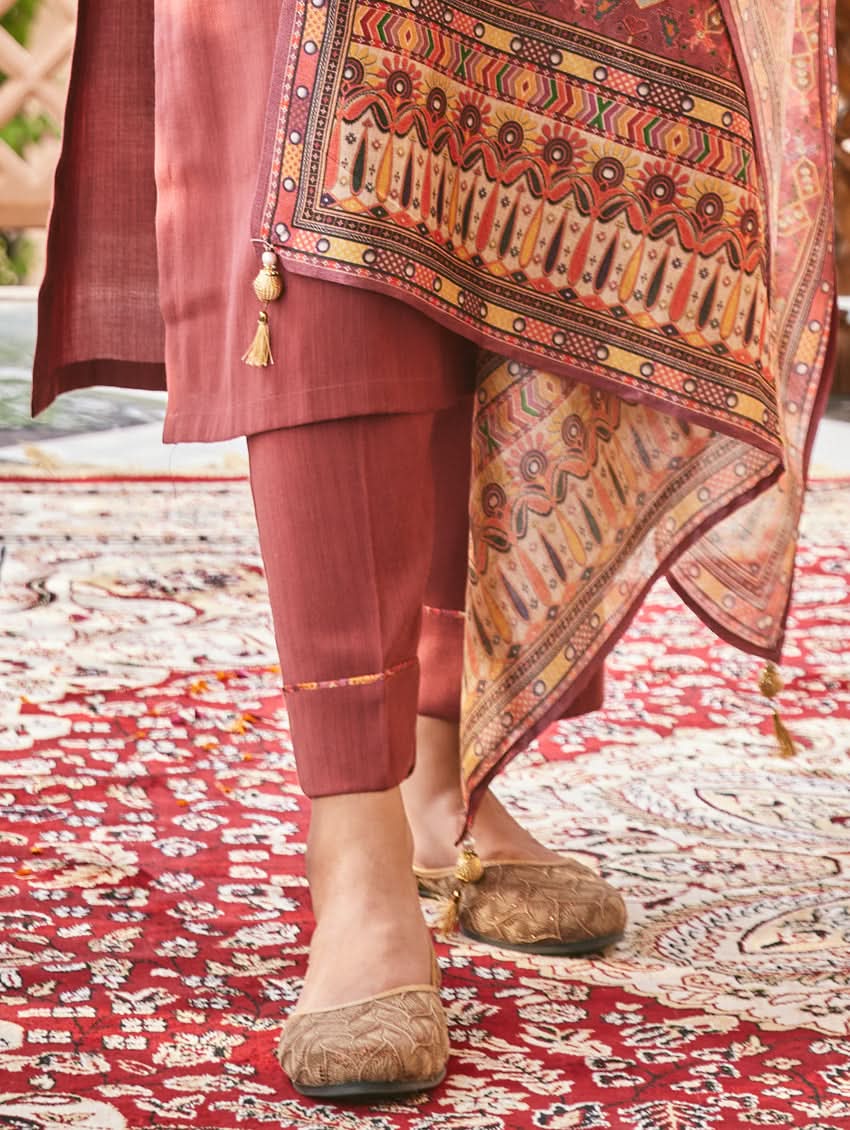 A woman standing in an elegant pose wearing a red silk suit set with floral patterns on the dupatta, straight pants, and a kurta with pearl work.