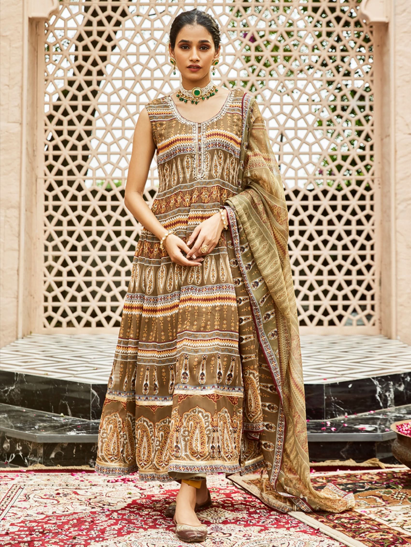 Woman in a traditional patterned dress standing in front of an ornate lattice.