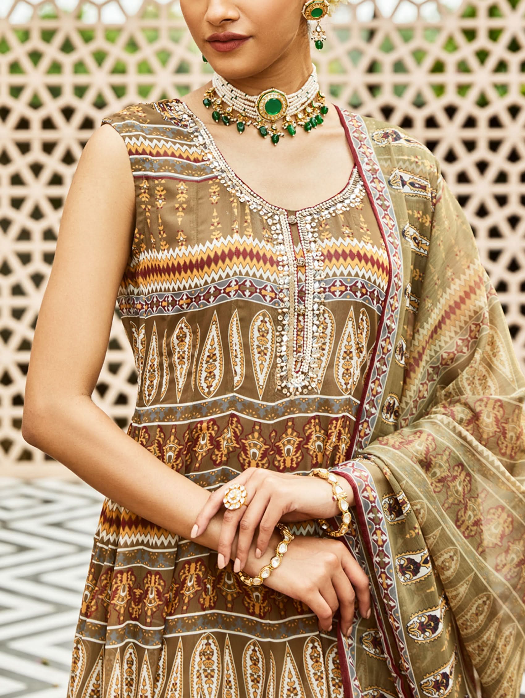 Woman wearing a traditional embroidered outfit with jewelry against a decorative wall.