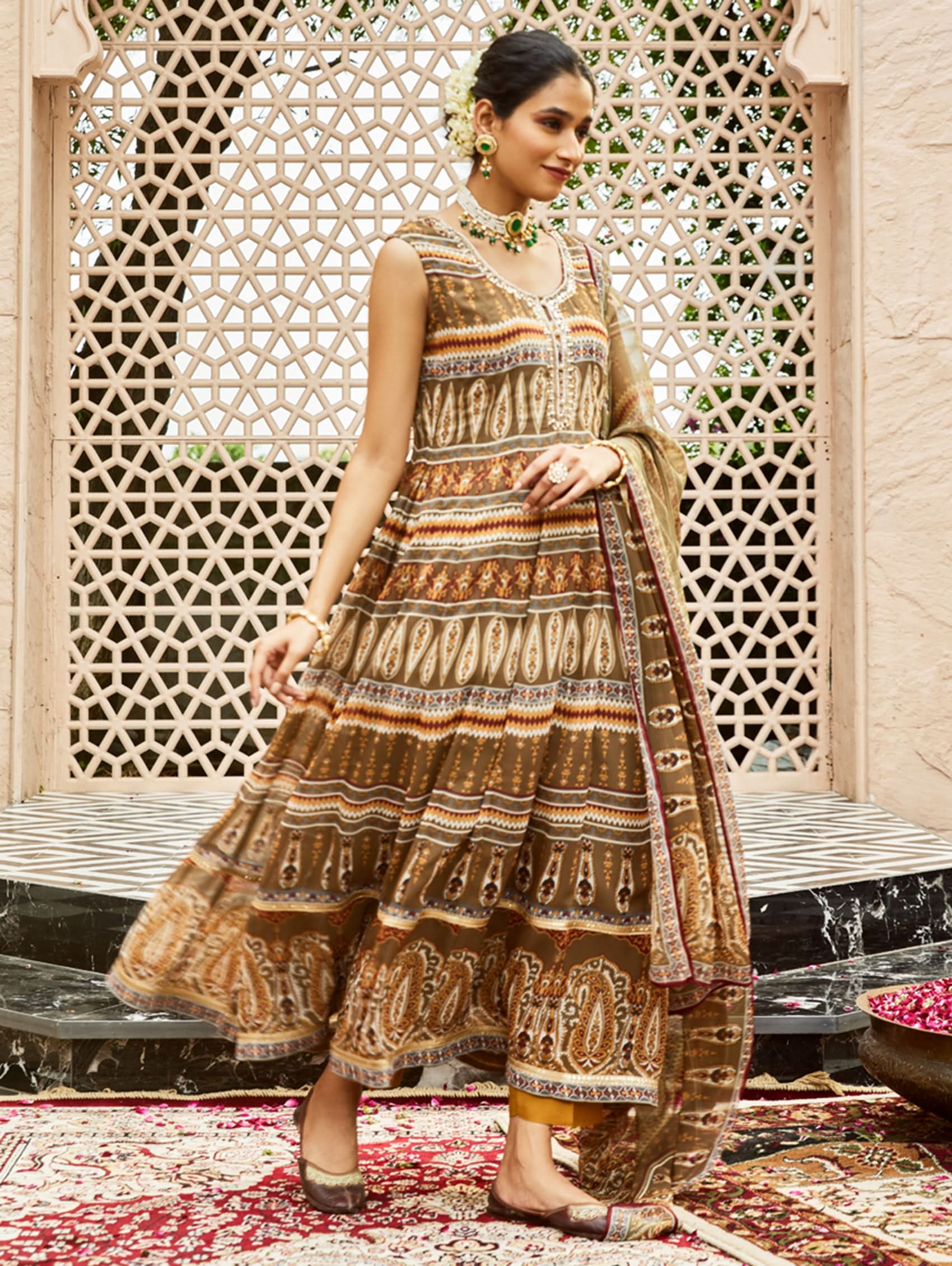 Woman in a patterned dress standing in front of an ornate lattice wall.