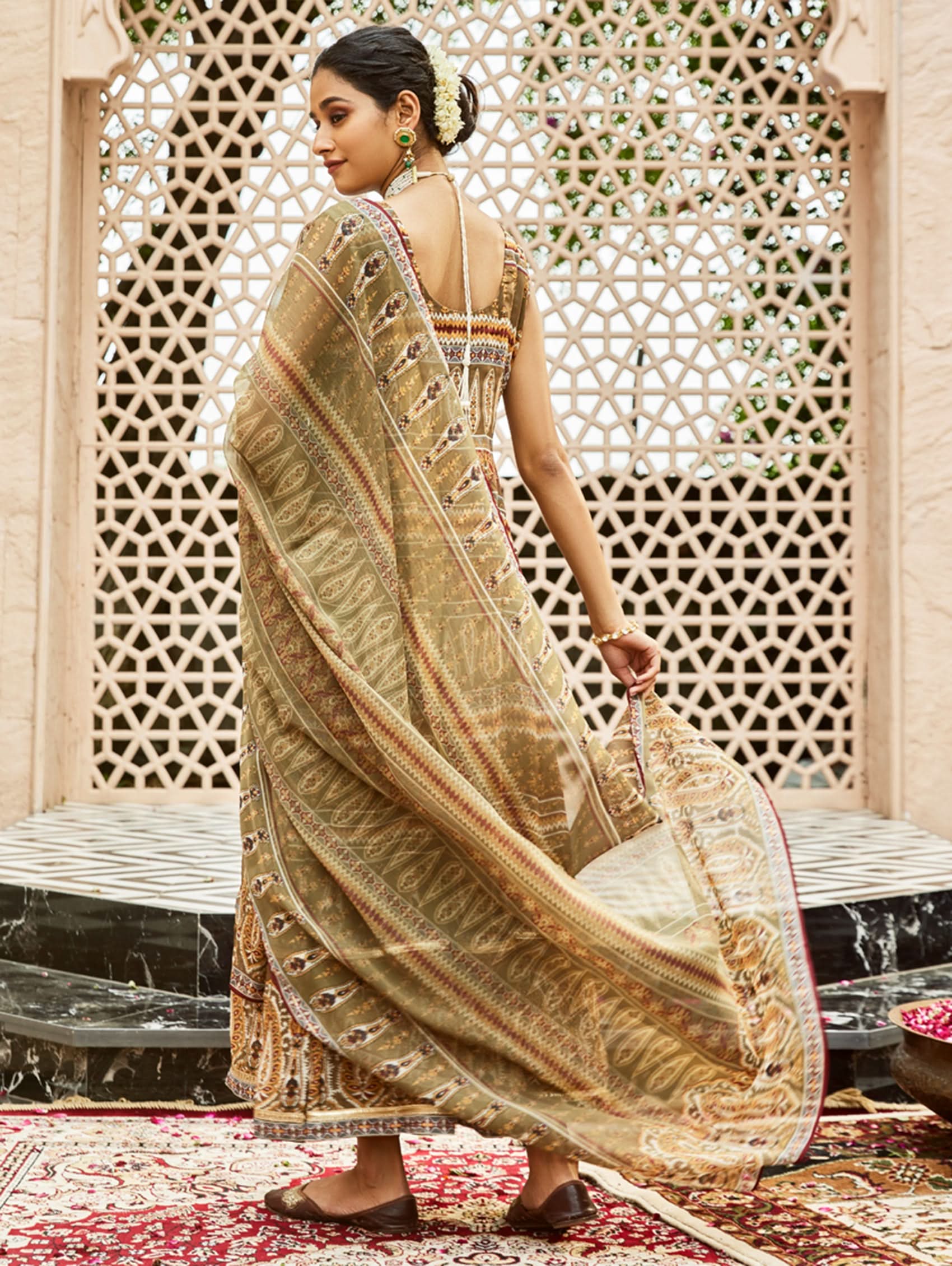 Woman in a traditional outfit standing in front of an ornate wall.