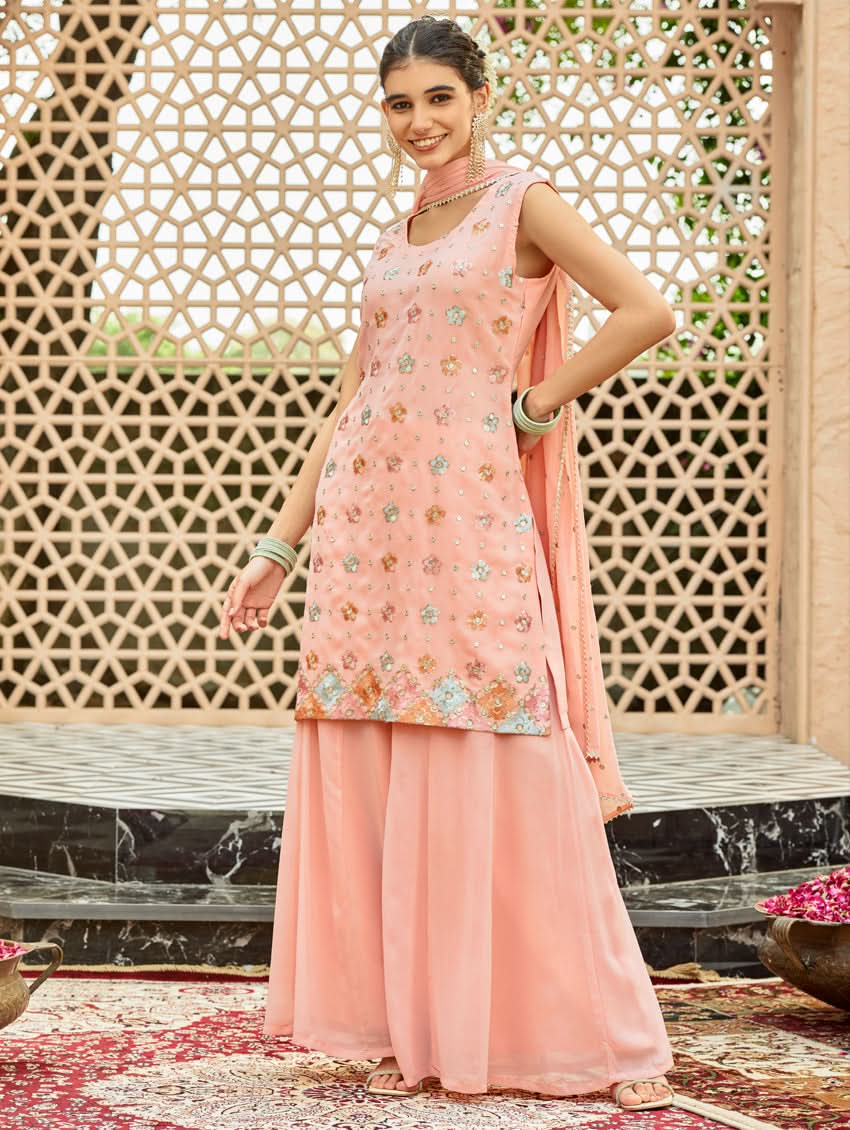 A model wearing a pink embroidered georgette sharara suit set with a round neckline and sleeveless design, featuring sequin work and a dupatta.