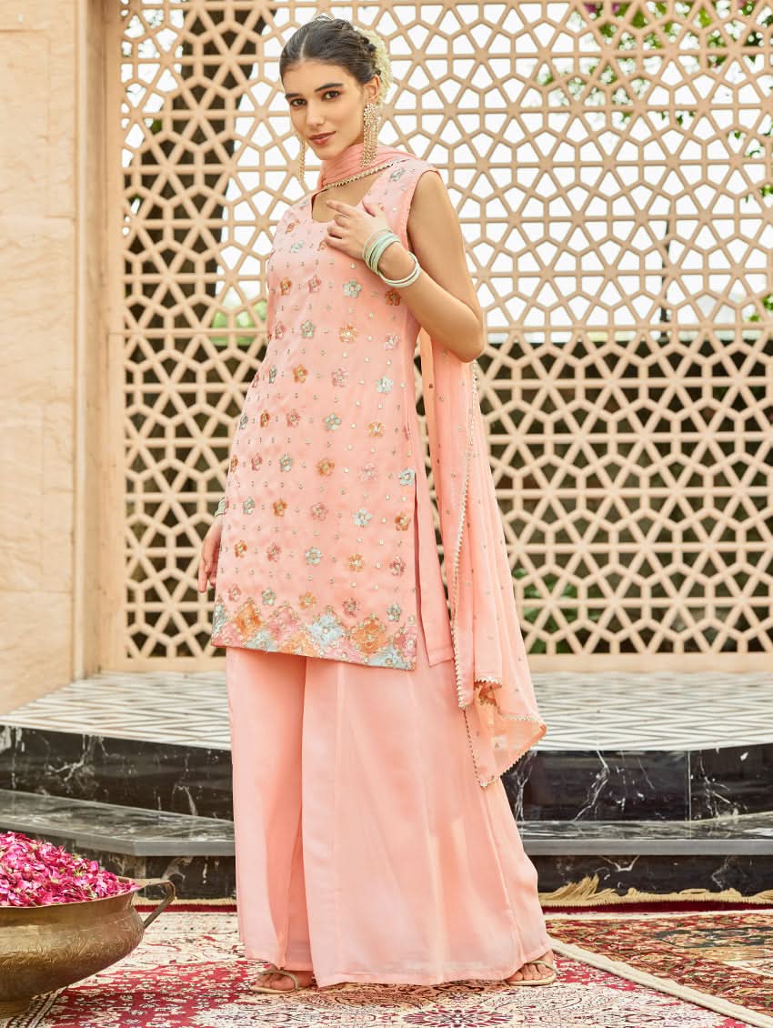 A model wearing a pink embroidered georgette sharara suit set with a round neckline and sleeveless design, featuring sequin work and a dupatta.